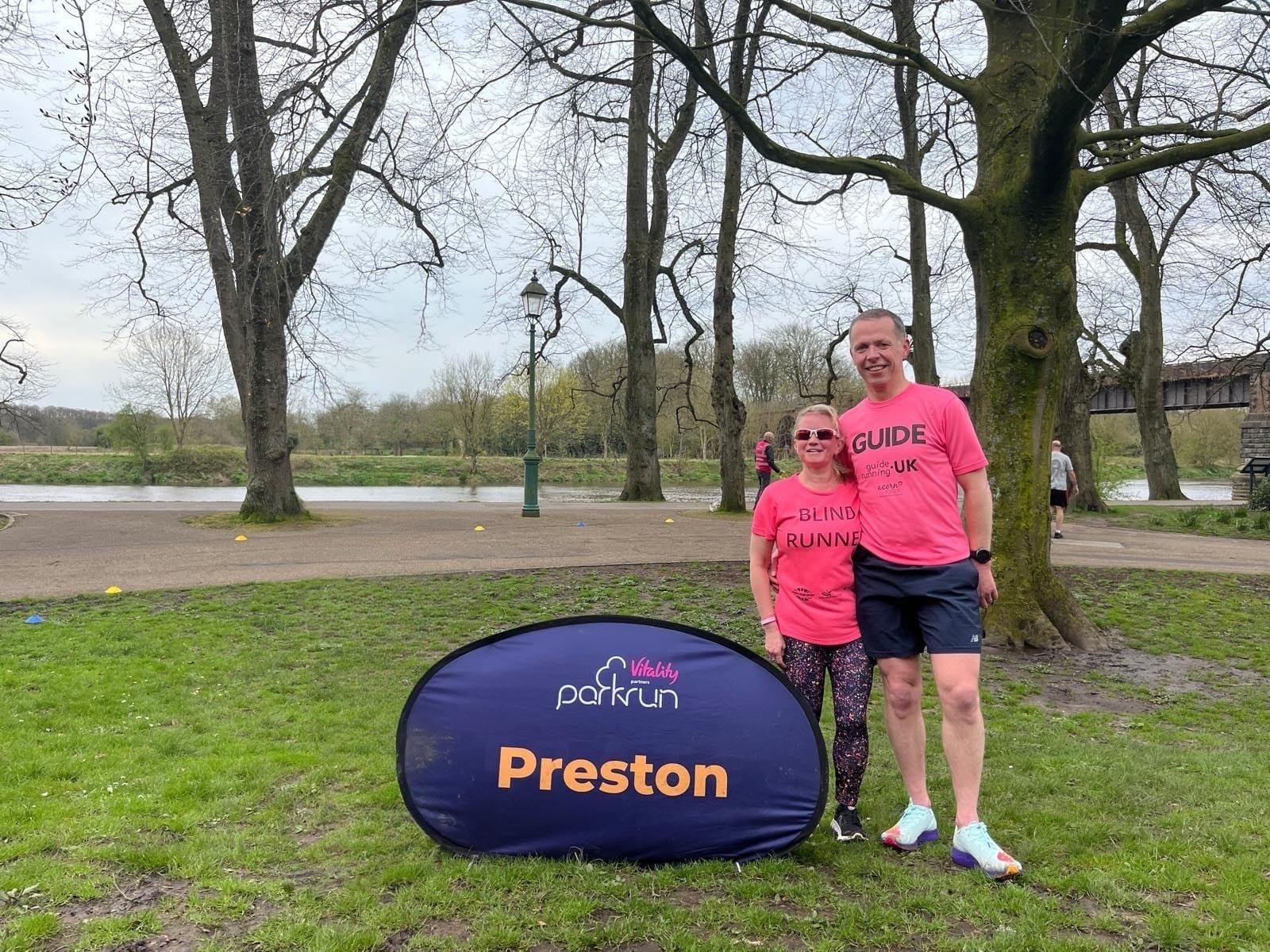 Kelly Barton, Engagement Manager for North West England, and husband Mike standing next to the Preston parkrun sign after finishing a parkrun there