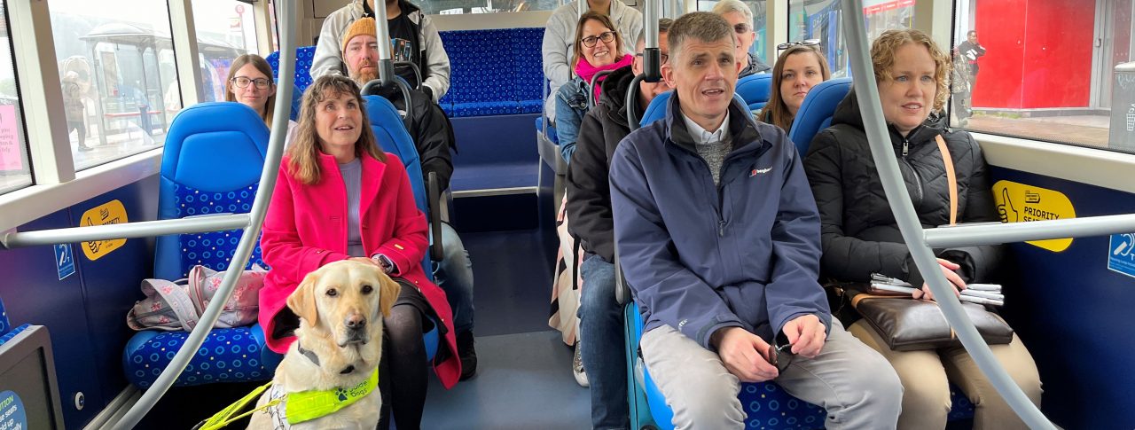 Sight Loss Council and Young Voices volunteers, and Thomas Pocklington staff, are sat on a bus creating some of the videos used in the training materials. Two passengers have white canes with them and there is a guide dog sat at the front.