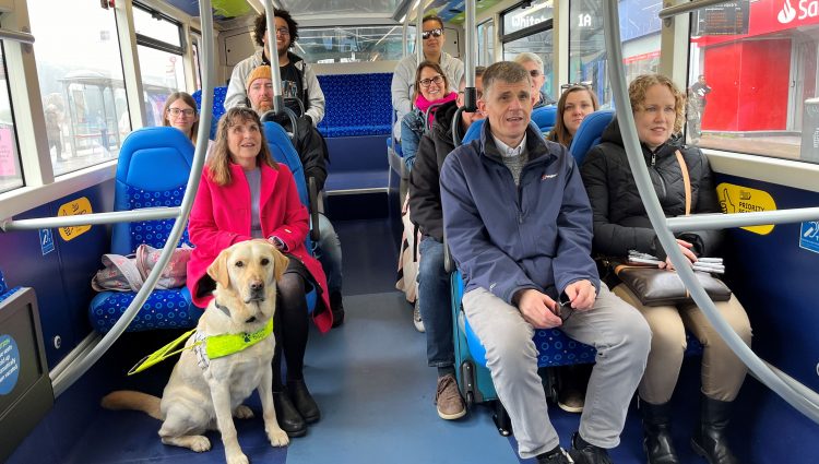 Sight Loss Council and Young Voices volunteers, and Thomas Pocklington staff, are sat on a bus creating some of the videos used in the training materials. Two passengers have white canes with them and there is a guide dog sat at the front.