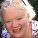 Dianne Flynne headshot. Diane has short blonde hair and is wearing a floral top. She is smiling at the camera.