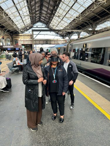 Six people standing on a railway platform at Preston train station, including members of Avanti West Coast and Community Rail Lancashire. A smartly dressed lady standing at the front of the group is wearing black sim specs.