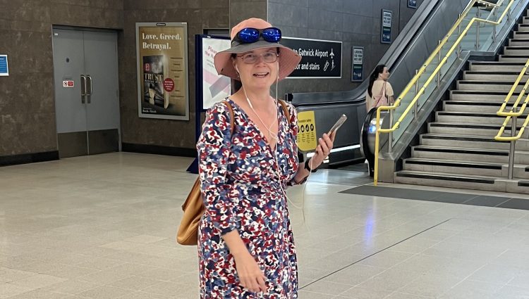 Vicky Blencowe, South West London SLC member, pictured at London Blackfriars train station. She is facing the camera, and holding her smartphone in her hand, whilst on the phone to an AIRA representative.