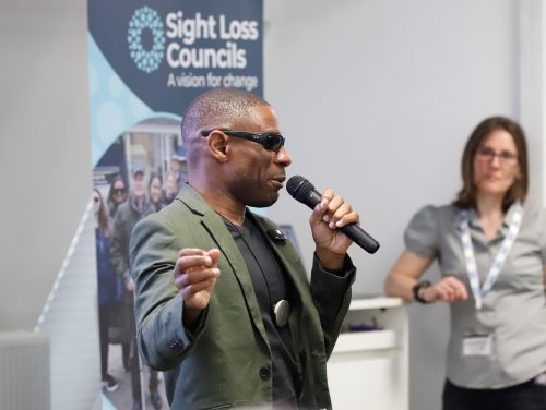Darren Harris, Darren Harris, double Paralympian and England footballer, talking into microphone infront of an SLC banner. TPT Director of Resources Louise is in the background.