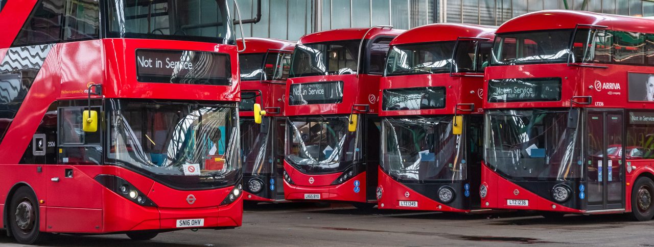 Row of four red double-decker buses parked in a line.