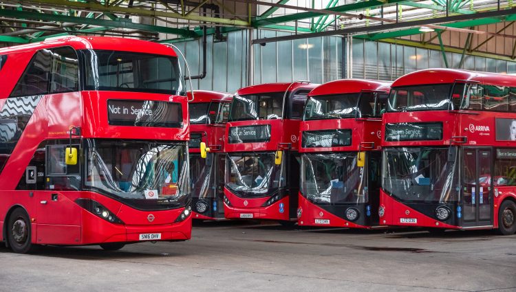 Row of four red double-decker buses parked in a line.