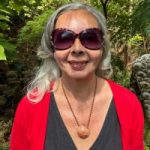 Patricia Clements headshot. Patricia has long light hair and is wearing a red cardigan and black top with a statement necklace and sunglasses. She is smiling at the camera.