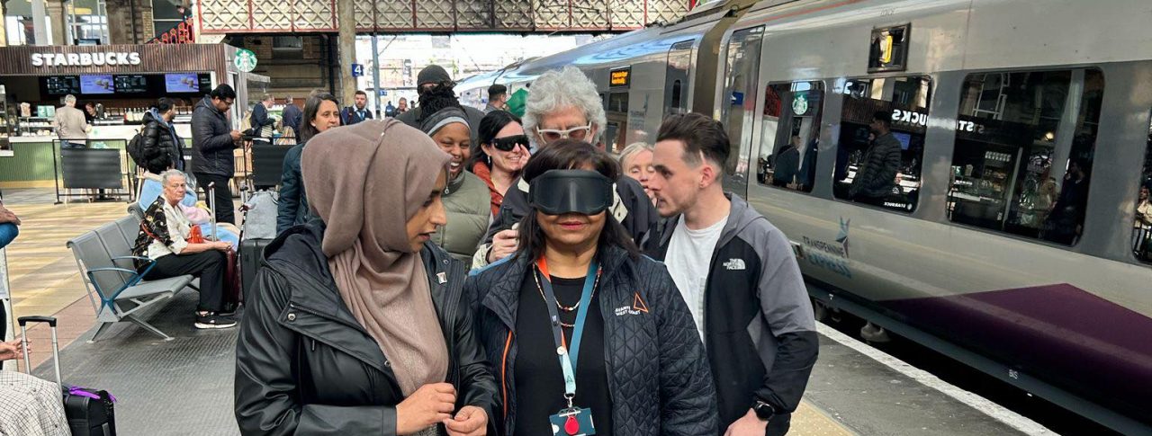 Six people standing on a railway platform at Preston train station, including members of Avanti West Coast and Community Rail Lancashire. A smartly dressed lady standing at the front of the group is wearing black sim specs.