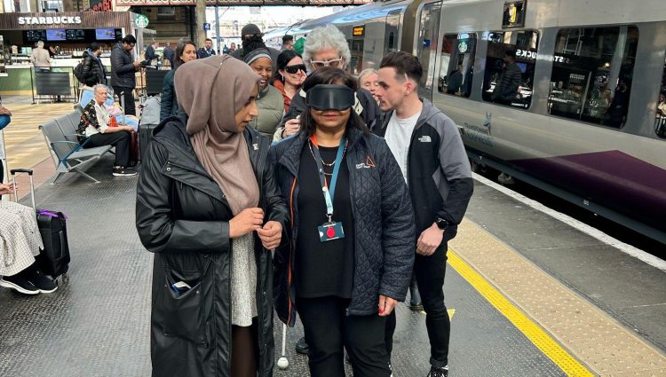 Six people standing on a railway platform at Preston train station, including members of Avanti West Coast and Community Rail Lancashire. A smartly dressed lady standing at the front of the group is wearing black sim specs.