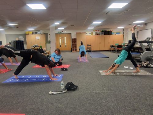 Five former Let's Get Active attendees participating in a yoga class. They are pictured doing the 'three legged downward dog' pose.