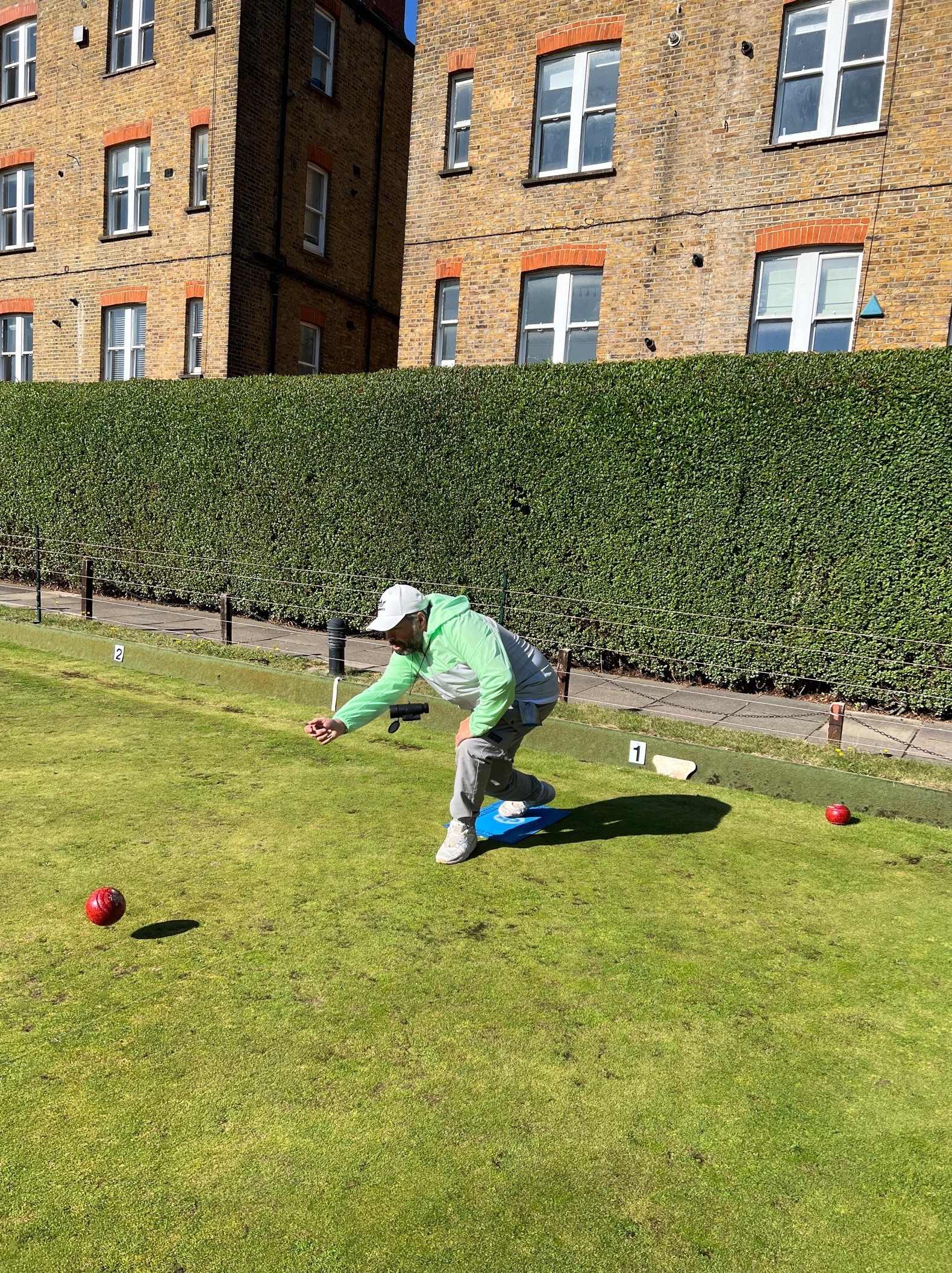 Portrait image of SE London volunteer, Steve, playing bowls on a bowling lawn. He is crouching down, having bowled his ball.