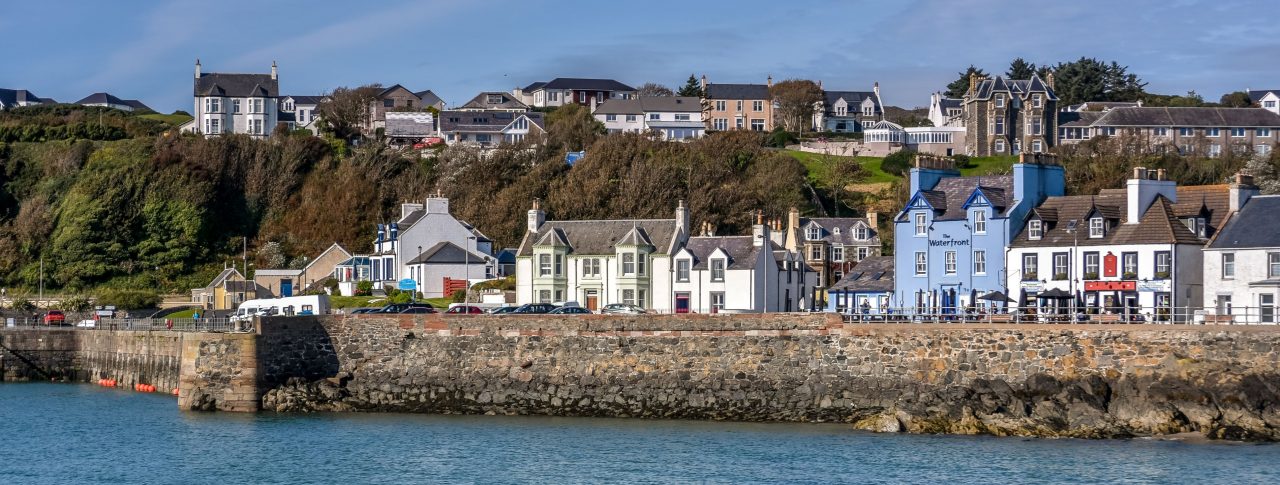 A row of pretty houses in a coastal down. A stone sea wall and the sea is in the foreground.